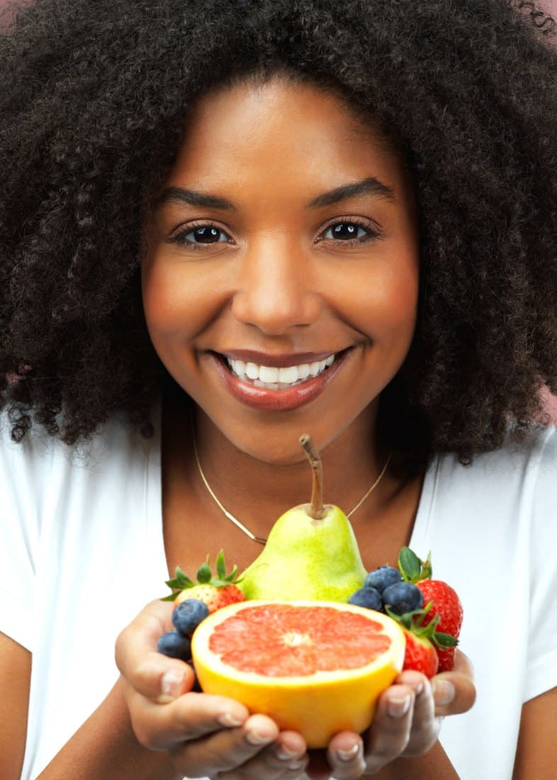 A smiling woman holding fresh grapefruit, pears, strawberries and blueberries
